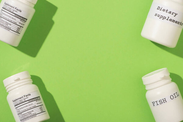 Top view of containers with fish oil and dietary supplements lettering on green background