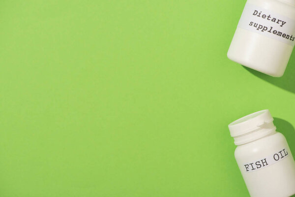 Вид сверху контейнеров с рыбьим жиром и диетическими добавками на зеленый
 