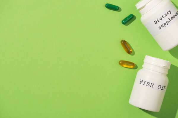 Top view of containers with fish oil and dietary supplements lettering with capsules on green 