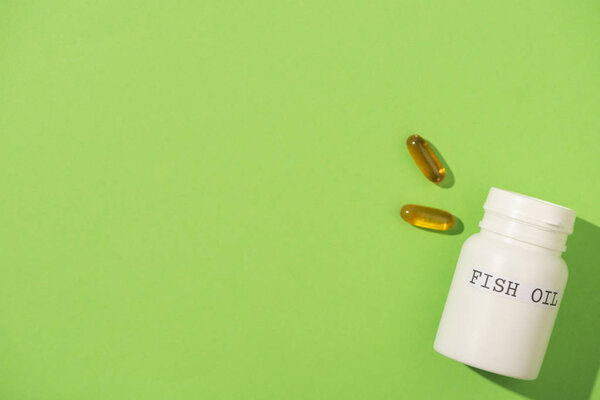 Вид сверху контейнера с рыбьим жиром и капсулами на зеленом
 
