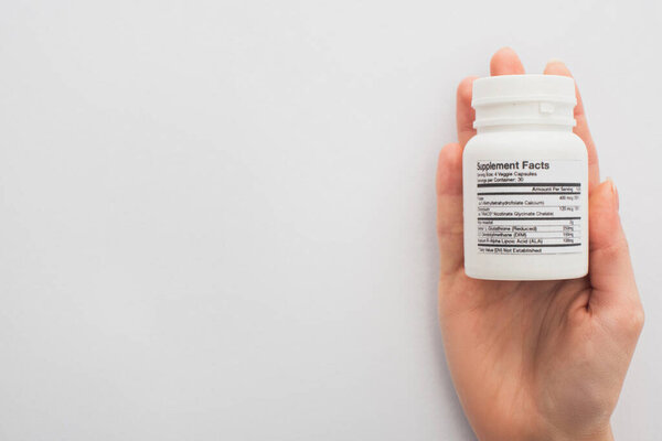 Cropped view of woman holding container with dietary supplements on white