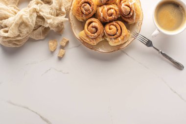 top view of fresh homemade cinnamon rolls on marble surface with cup of coffee, fork and cloth clipart