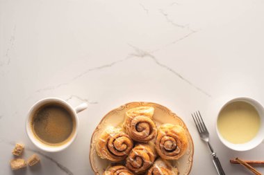 top view of fresh homemade cinnamon rolls on marble surface with cup of coffee, condensed milk, fork clipart
