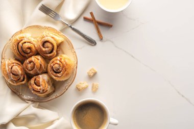 top view of fresh homemade cinnamon rolls on marble surface with coffee, condensed milk, fork and satin cloth clipart