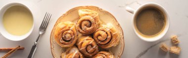 top view of fresh homemade cinnamon rolls on marble surface with cup of coffee, fork and condensed milk, panoramic shot clipart