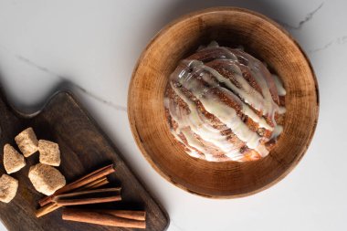 top view of fresh homemade cinnamon roll on plate on marble surface with cutting board with brown sugar, cinnamon sticks clipart