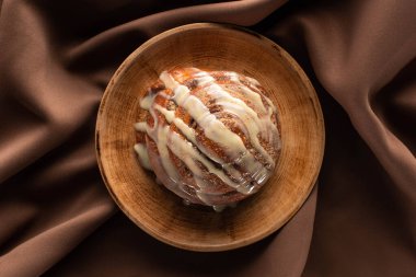 top view of fresh homemade cinnamon roll on plate on silk brown cloth clipart