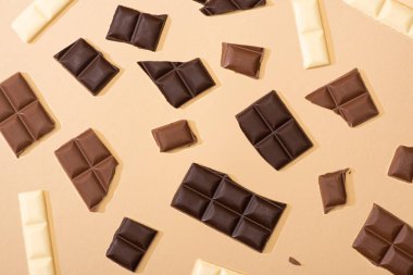 top view of delicious dark, milk and white chocolate pieces on beige background clipart