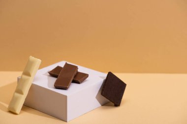 Lezzetli beyaz, koyu ve sütlü çikolata parçaları ve bej arka planda küp