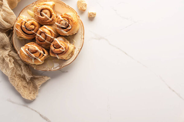 top view of fresh homemade cinnamon rolls on marble surface with brown sugar and cloth