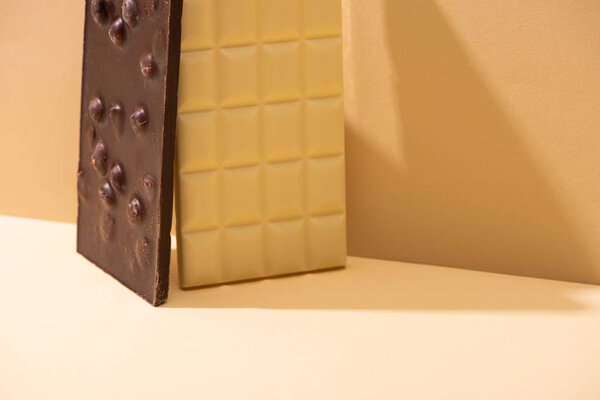 вкусные белые и темные шоколадные батончики с орехами на бежевом фоне
