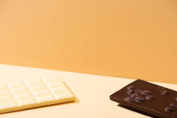 вкусные сломанные белые и темные шоколадные батончики с орехами на бежевом фоне
