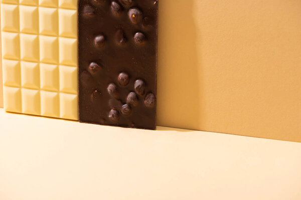 вкусные сломанные белые и темные шоколадные батончики с орехами на бежевом фоне
