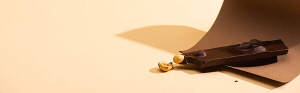 delicious dark chocolate with nuts piece, paper on beige background, panoramic shot