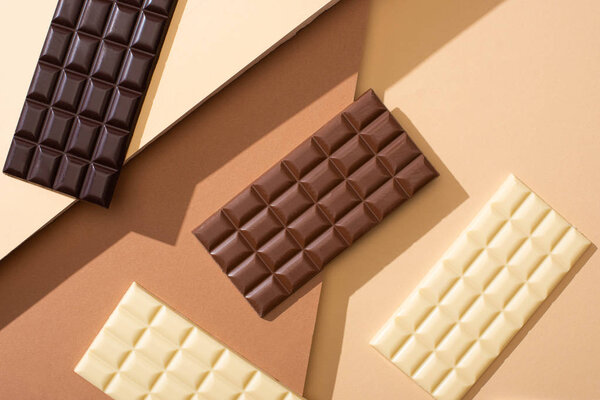 top view of delicious whole milk, white and dark chocolate bars on beige background