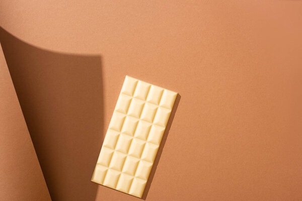 selective focus of delicious whole white chocolate bar on brown background with paper