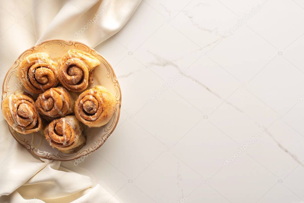 top view of fresh homemade cinnamon rolls on marble surface with silk cloth