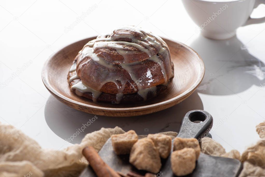 selective focus of fresh homemade cinnamon roll on plate near cutting board with brown sugar and cinnamon