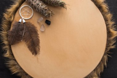 Top view of smudge sticks, crystals and dreamcatcher on tambourine on dark wooden background clipart