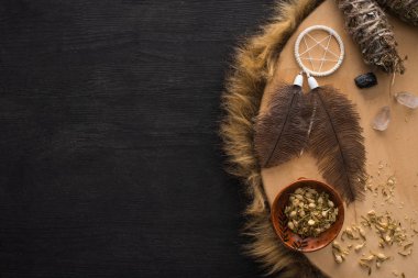 Koyu ahşap yüzey üzerindeki şamanik tef üzerinde tüyleri ve kristalleri olan rüya yakalayıcının yanındaki leke izlerinin üst görüntüsü.