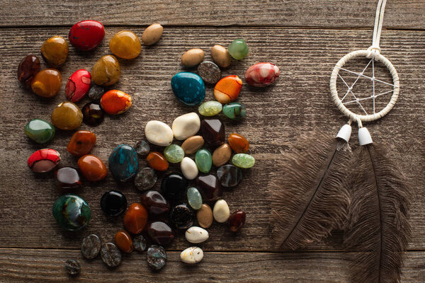 Top view of fortune telling stones and dreamcatcher with feathers on wooden surface