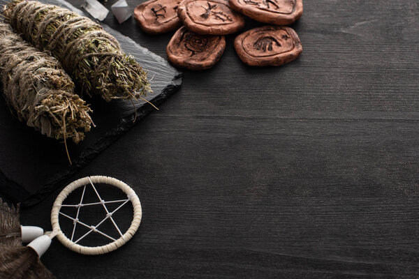 Herbal smudge sticks, dreamcatcher and clay amulets on dark wooden background