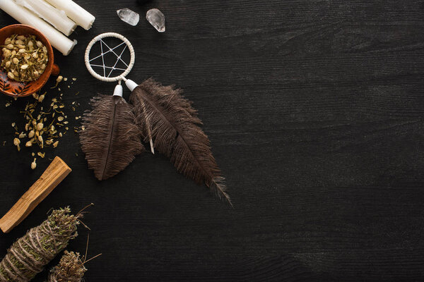 Top view of dreamcatcher, smudge sticks with magical crystals and candles on dark wooden surface