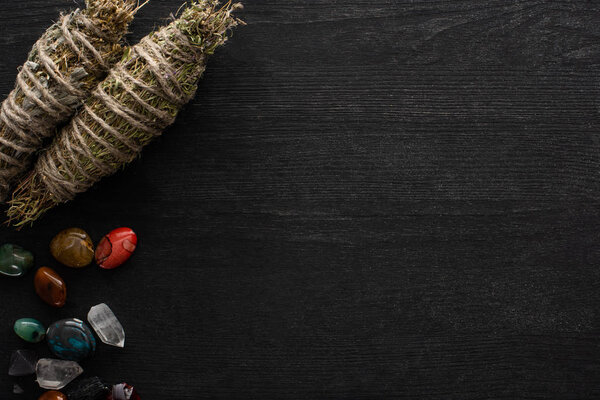 Top view of shamanic smudge sticks with fortune telling stones on black wooden surface