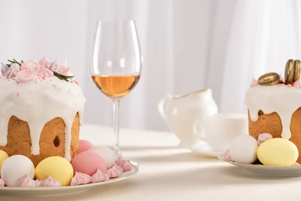 プレートの上にカラフルな卵とワイングラスの近くにメレンゲで飾られたおいしいイースターケーキ — ストック写真