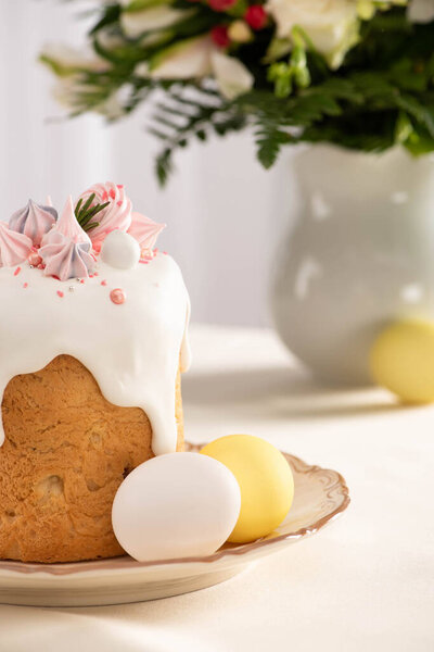 селективный фокус вкусного пасхального торта, украшенного безе возле красочных яиц на тарелке с вазой цветов
