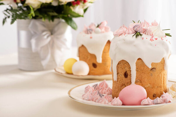 selective focus of festive Easter cake decorated with meringue near painted eggs on plates and flowers