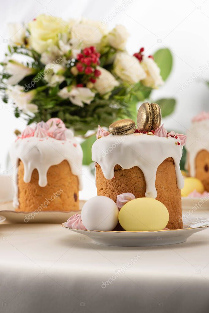 selective focus of delicious easter cake with golden french macaroons and meringue on icing near floral bouquet and eggs