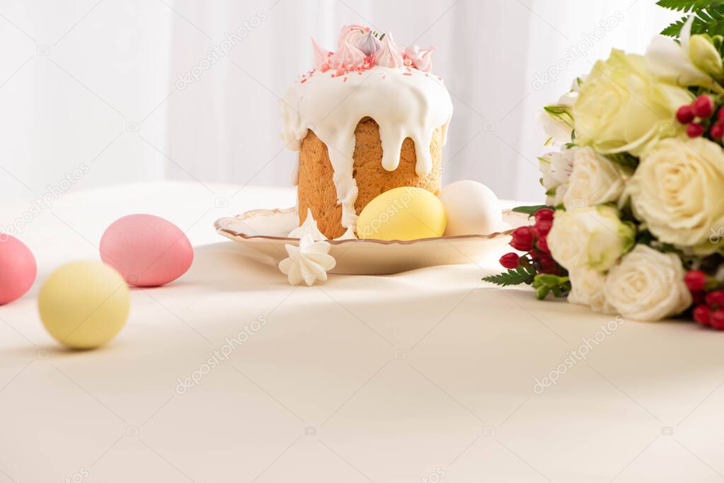 delicious Easter cake decorated with meringue with colorful eggs on plate near flowers