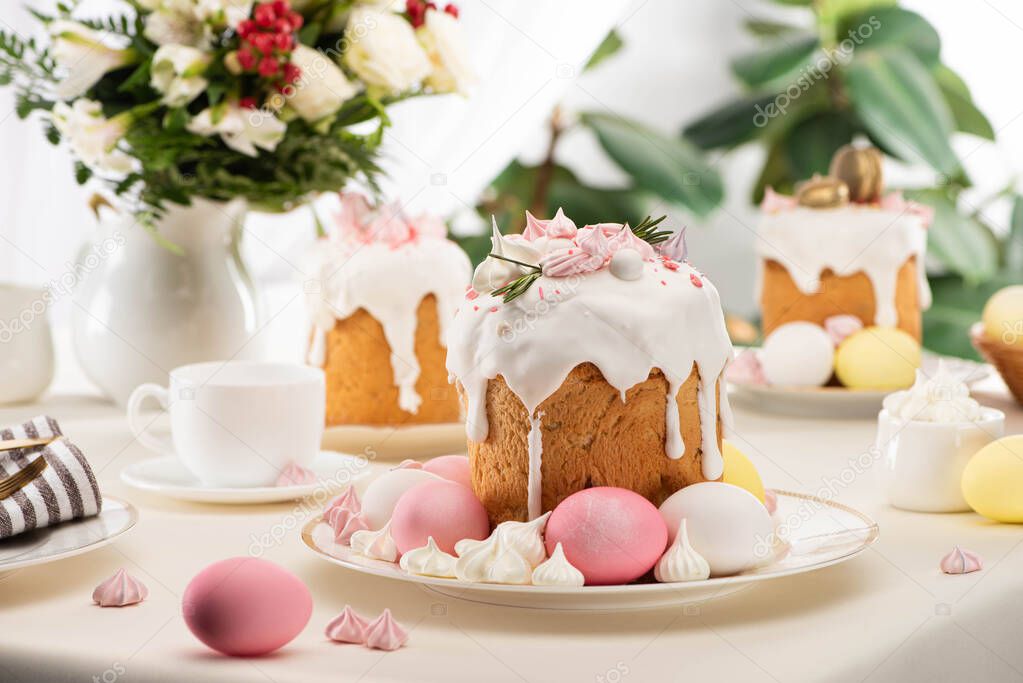 selective focus of Easter cakes with colorful eggs near flowers in vase on table