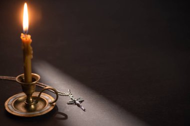 church candle in candlestick burning near catholic cross in dark with sunlight clipart