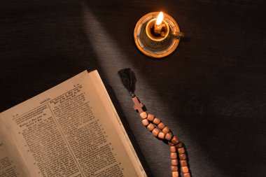 KYIV, UKRAINE - JANUARY 17, 2020: top view of open holy bible with rosary and candle on dark background with sunlight