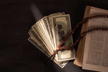 KYIV, UKRAINE - JANUARY 17, 2020: top view of holy bible with money and rosary on dark background with sunlight