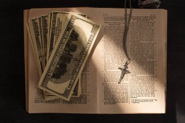 KYIV, UKRAINE - JANUARY 17, 2020: top view of holy bible with money and cross on dark background with sunlight