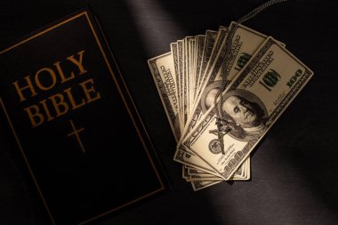 top view of holy bible with money and cross on dark background with sunlight clipart