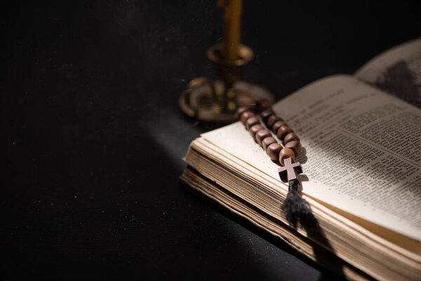KYIV, UKRAINE - JANUARY 17, 2020: selective focus of candlestick near bible with catholic rosary in dark with sunlight