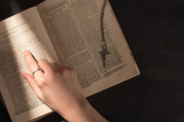 KYIV, UKRAINE - JANUARY 17, 2020: partial view of woman reading holy bible near cross in dark