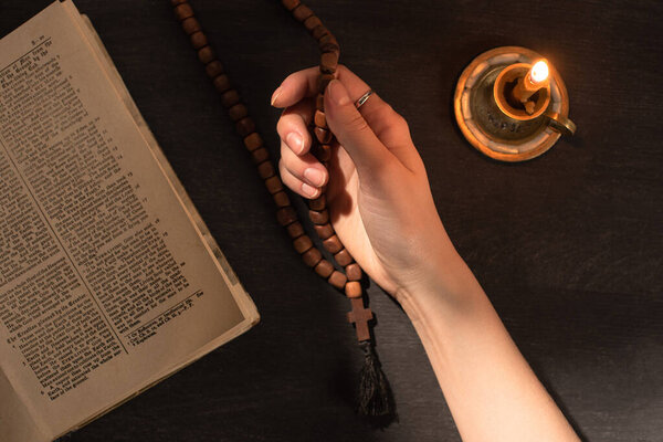 KYIV, UKRAINE - JANUARY 17, 2020: cropped view of woman praying with rosary near open holy bible and candle