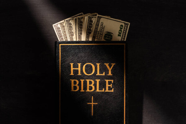 top view of holy bible with money on dark background with sunlight