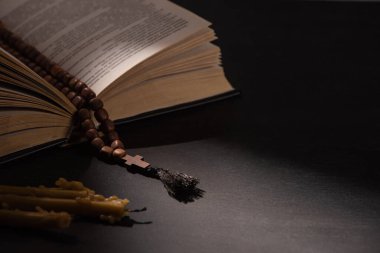 holy bible with rosary on black dark background with candles clipart