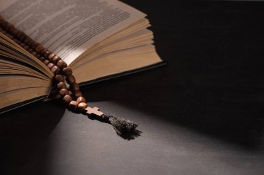 Kara arka planda güneş ışığıyla tespih çeken kutsal İncil. 