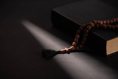 Kara arka planda güneş ışığıyla tespih çeken kutsal İncil. 