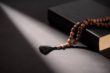 Kara arka planda güneş ışığıyla tespih çeken kutsal İncil. 