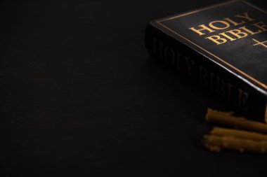 selective focus of holy bible and candles on black dark background clipart