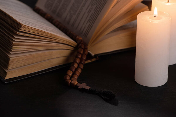 Священная Библия с четками на черном темном фоне с горящими свечами
