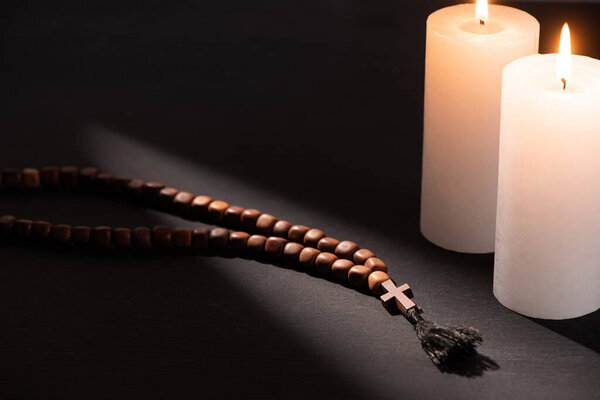 rosary on black dark background with burning candles